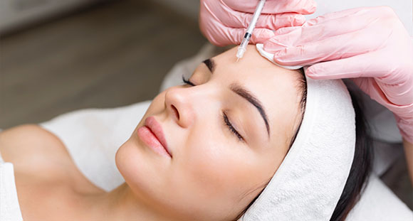 a woman receiving an anti-wrinkle injection to her forehead from a pink-gloved beautician
