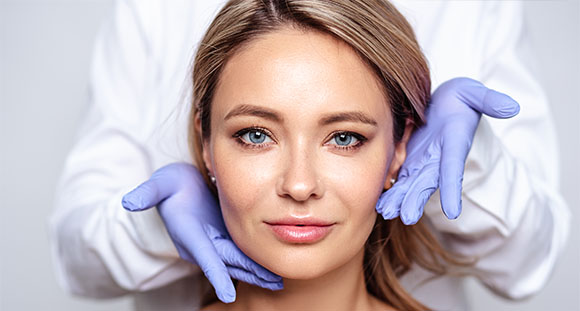 a gloved doctor holding their hands around the face of a woman who has received a new anti-wrinkle treatment