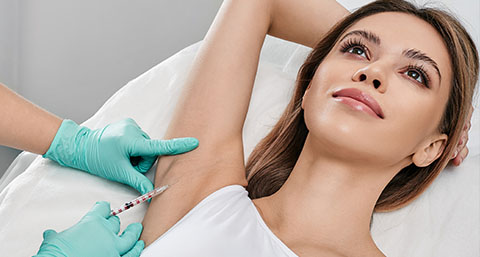 a woman holding her arm up receiving an injection to the underarm for an axillary hyperhidrosis treatment